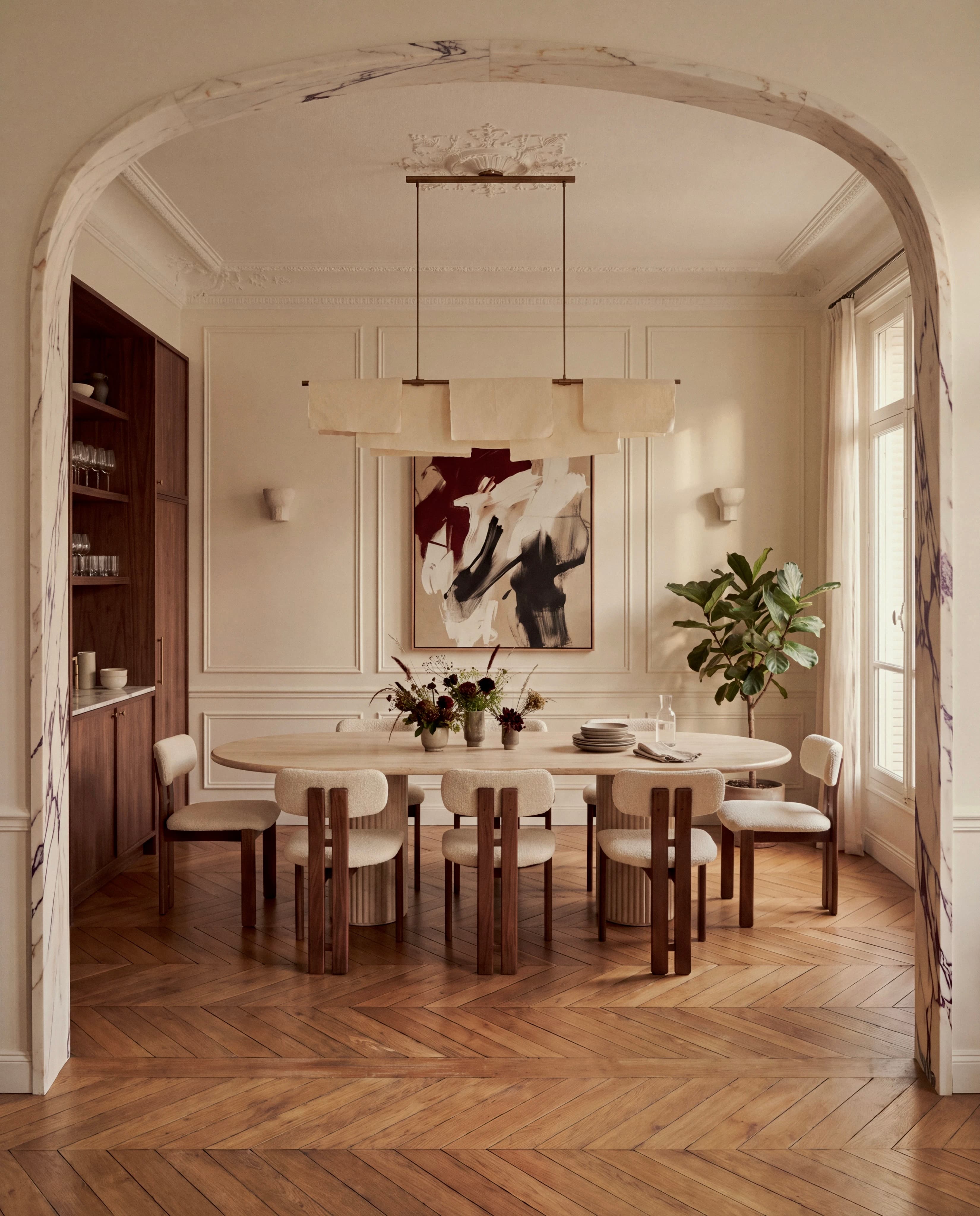 Dining room seen through a marble arch, with an oval table, upholstered chairs and a linear pendant